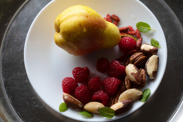 ORGANIC FRESH PEAR ON WHITE PLATE WITH WATER DROPLET RASPBERRIES NUTS MINT GARNISH 