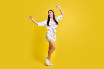 Fototapeta na wymiar Full length photo of charming relaxed young lady look empty space raise hands isolated on yellow color background