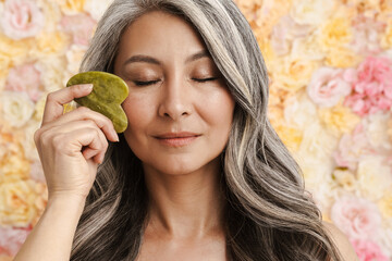 Mature woman massaging face with jade roller standing