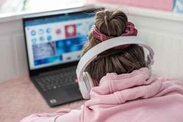 Nauka zdalna w domu podczas pandemii covid-19, Dziewczynka pracuje na komputerze ze słuchawkami na uszach, nauka przez komputer, zamknięte szkoły - obrazy, fototapety, plakaty
