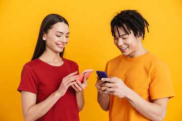 Young multiracial couple smiling and using mobile phones