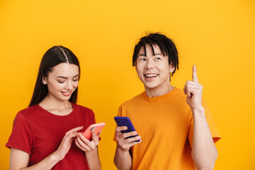 Young multiracial couple pointing finger upward and using cellphones
