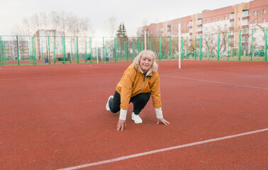 Fototapeta premium an elderly woman in a yellow jacket is doing sports exercises on a red treadmill. the stadium is a healthy lifestyle. retired people and sports.