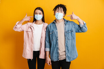 Young multiracial couple pointing fingers at their face masks