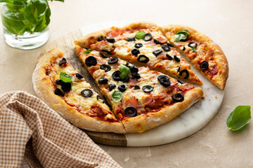 Homemade pizza ham, black olives, cheese and fresh basil. Sourdough pizza.