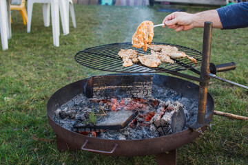 Fire ring and poultry meat on grill and human hand with fork. Grilling season and summer.