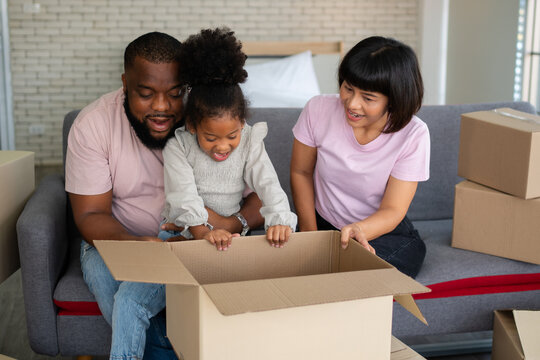 Mixed Race Families Are Sitting On The Sofa And Surprised After Open The Gift Box From A Neighbor On The First Day After Moving House.  Concept Of Starting A New Life For A New Family.