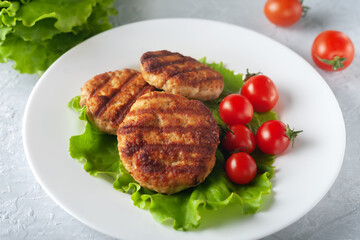 Fried cutlet with salad and tomatoes in a white plate on a gray background