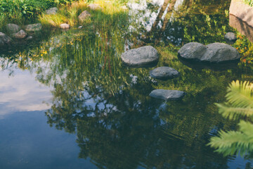 Pond water stones landscape Wet stones by mood lake shore. Sky in reflection. Beautiful small garden pond with stone shores. Balance harmony relaxation and peace concept. Scenic photo, copy space