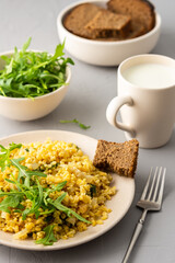 Delicious bulgur porridge with fried onions and herbs in a plate, a glass of milk, arugula in a bowl and black bread