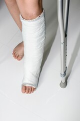 Detail left leg or in white plaster placed and crutch.Broken leg in plaster. The boy has a broken ankle.