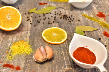 Spices and seasonings with garlic, bay leaf, black pepper peas and lemon slices, and a bowl of red paprika on a gray table