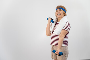 An elderly woman with a blue bandage on her head trains with dumbbells on a white background