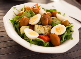 dish of fresh vegetables arugula, avocado, cherry tomatoes with olives and quail eggs on dining table