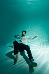 Fototapeta na wymiar Muslim man in formal wear swimming underwater with closed eyes