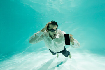 Amazed arabian businessman holding smartphone with blank screen underwater