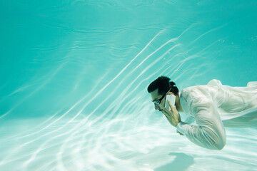 Muslim businessman in goggles talking on cellphone underwater in pool