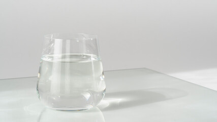 Glass of fresh pure water on white background with sunlight and deep shadow of glass. Hard sunlight.