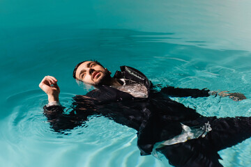 Arabian businessman in formal wear looking away while swimming in pool