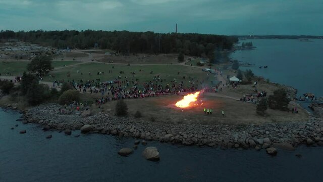Bonefire midsummer nearby the sea surrounded by people Helsink, Kotka Finland top view. drone high angle movement. beautiful sunset people enjoy the warm weather