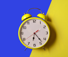 Illuminating color Retro style alarm clock on blue and yellow background.