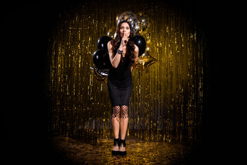 Full size photo of brown optimistic lady stand hide balloons wear black dress shoes isolated on dark gold color background in stage light