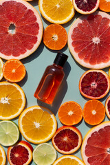 Vitamin C serum in a glass bottle on a slised citrus set. Orange, grapefruit, lime, tangerine, lemon. Organic SPA cosmetics with orange oil.