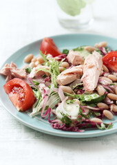 Tuna salad with tomatoes, cannelloni bean and endive. Bright wooden background. Close up.