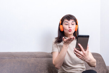 Fototapeta premium Charming brunette woman wearing orange headphones having a video call and sending a kiss.