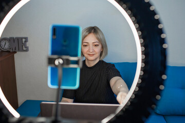 Video blogging. Business style woman talking to camera and recording video with smartphone and ring light lamp at home, working from home concept, social distant reality