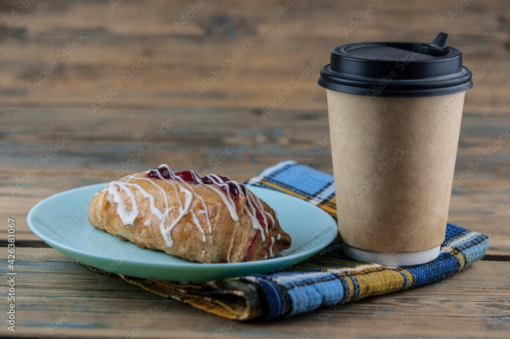 Wall mural On a table made of natural wooden boards there is a ceramic plate with a sweet cherry bun. Breakfast