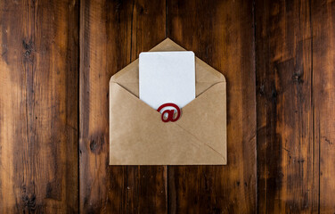 An email sign with white blank paper on a craft envelope lies on a vintage wooden table. Concept e-mail message letter. Top view with copy space