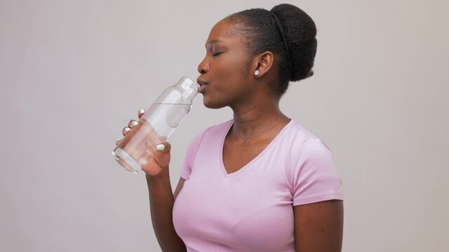 people concept - portrait of happy smiling young african american woman drinking water from reusable glass bottle over grey background