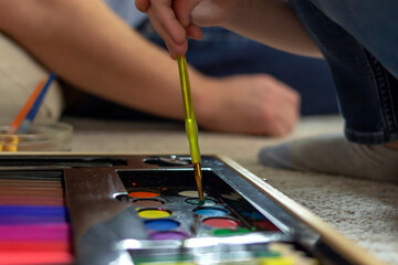 Children hand with paint brush beginning to create. Close up of sweet little artist hand mixing water paint with brush. Shot of hands and brush paint watercolor, sitting at home.