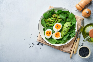 Fresh vegetable salad with avocado, asparagus, crumpled eggs with black sesame seeds and spinach on plate on light slate, stone or concrete background. Balanced lunch in bowl. Top view. Mock up.