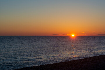 colorful sunset with a cloudless sky overlooking the sea and the setting bright sun