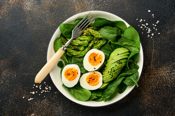 Fresh vegetable salad with avocado, asparagus, crumpled eggs with black sesame seeds and spinach on plate on light slate, stone or concrete background. Balanced lunch in bowl. Top view. Mock up.