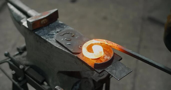 Blacksmith bends a red-hot metal rod on an anvil into a spiral, decorative blacksmith craft, forged metal, 4k 60p Prores HQ