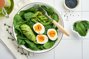 Fresh vegetable salad with avocado, asparagus, crumpled eggs with black sesame seeds and spinach on plate on light slate, stone or concrete background. Balanced lunch in bowl. Top view. Mock up.
