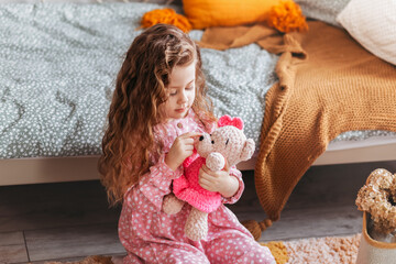 Little cute girl plays with soft toy bear on the floor in the children's bedroom