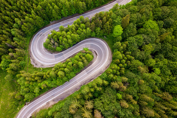 Aerial view of winding road in high mountain pass trough dense green pine woods.