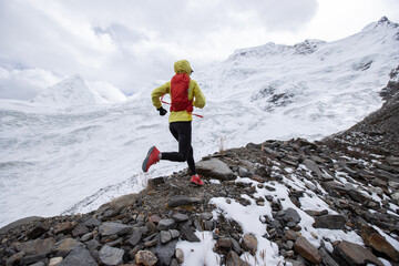 Woman trail runner cross country running up hill to winter snow mountain top