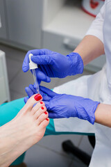 Pedicure master applies care product to nails of young woman in nail salon. Nail care.