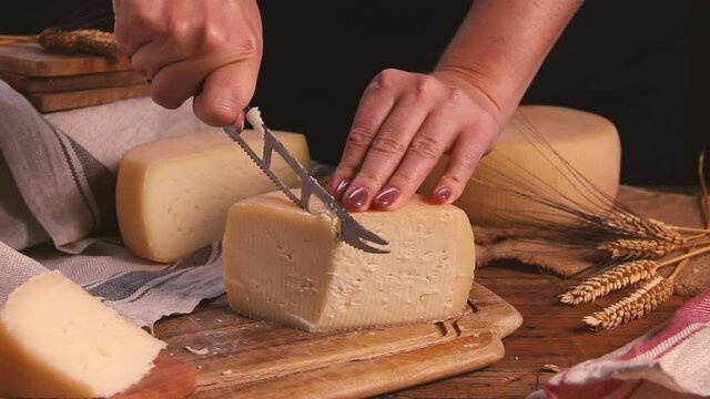 Women cut fresh homemade cheese on a wooden board with a cheese knife close up
