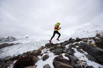 Woman trail runner cross country running up hill to winter snow mountain top