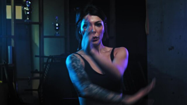 Tattooed woman stands in fighting pose and showing her karate moves in neon lighting