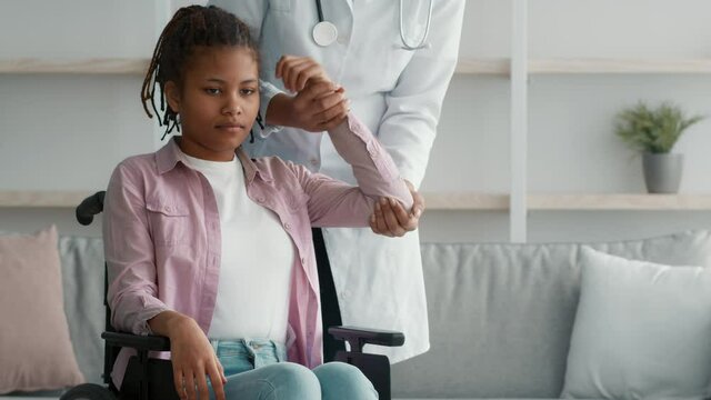 Doctor Physiatrist Massaging Arm Of Handicapped Girl In Wheelchair Indoors