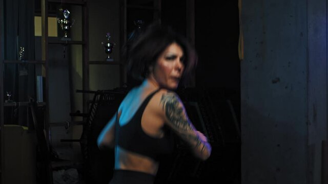 A strong tattooed woman stands in fighting pose and showing her karate moves in neon lighting