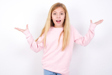 beautiful caucasian little girl wearing pink hoodie over white background raising hands up, having eyes full of happiness rejoicing his great achievements. Achievement, success concept.