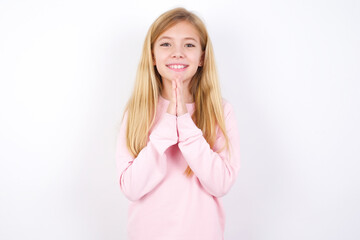 beautiful caucasian little girl wearing pink hoodie over white background keeps palms together, has...